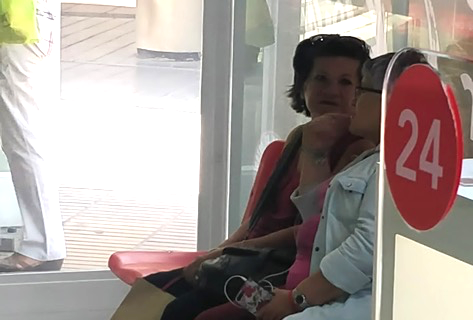 A store customer resting in the seating area during a long counter interaction.